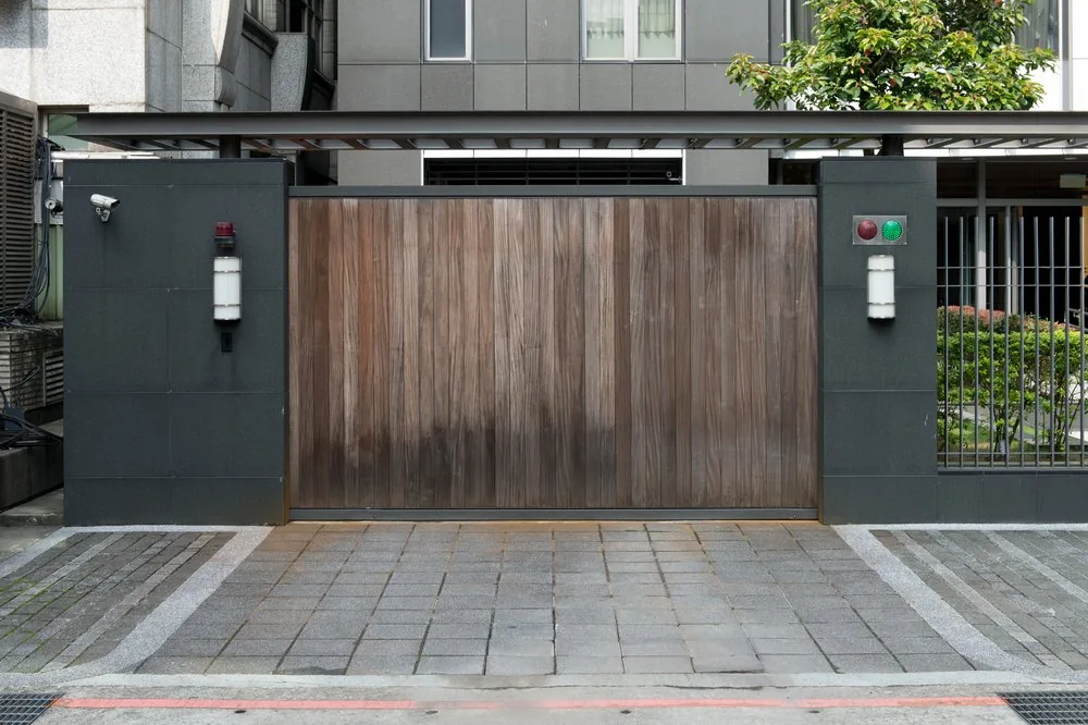 Wood-panel sliding gate between dark posts with keypad and lights